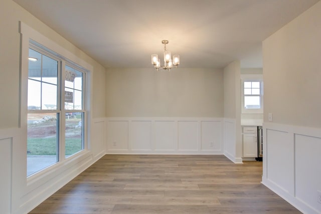 spare room with plenty of natural light, light hardwood / wood-style flooring, and a notable chandelier