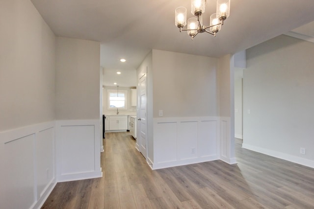 unfurnished dining area featuring light wood-type flooring, sink, and an inviting chandelier