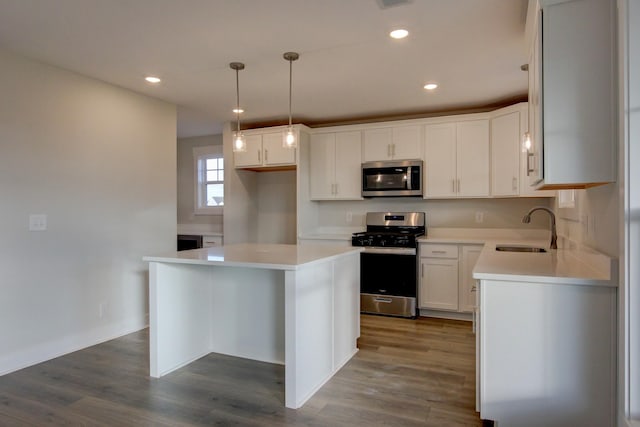 kitchen featuring white cabinets, sink, appliances with stainless steel finishes, decorative light fixtures, and a kitchen island