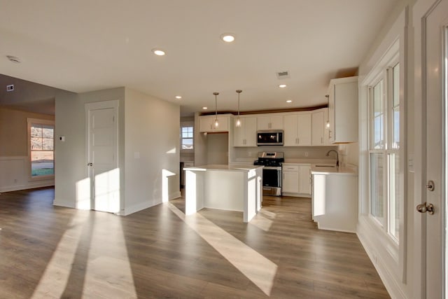 kitchen featuring white cabinets, hanging light fixtures, a kitchen island, wood-type flooring, and stainless steel appliances