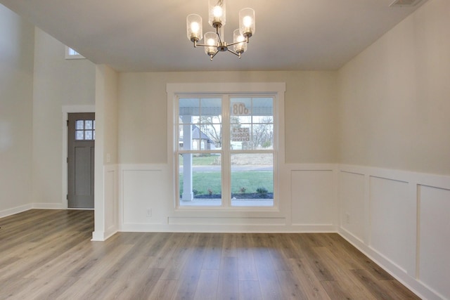 unfurnished dining area with wood-type flooring and an inviting chandelier