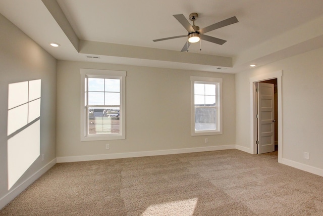 carpeted spare room with ceiling fan, a wealth of natural light, and a tray ceiling