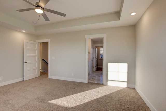 unfurnished bedroom featuring ceiling fan, carpet floors, and a tray ceiling