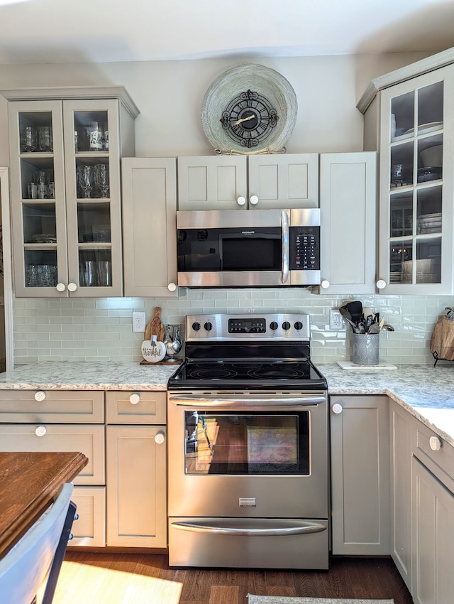 kitchen featuring hardwood / wood-style floors, light stone countertops, backsplash, and appliances with stainless steel finishes