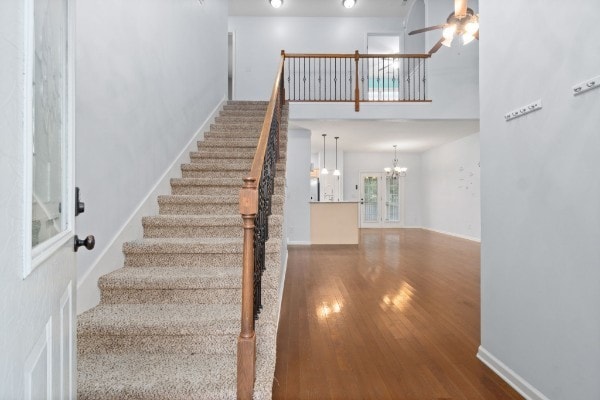 stairs with hardwood / wood-style floors, a towering ceiling, and ceiling fan