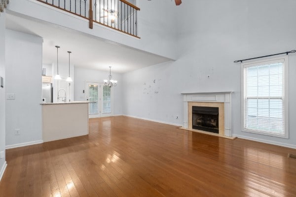 unfurnished living room featuring hardwood / wood-style flooring, a towering ceiling, and ceiling fan with notable chandelier