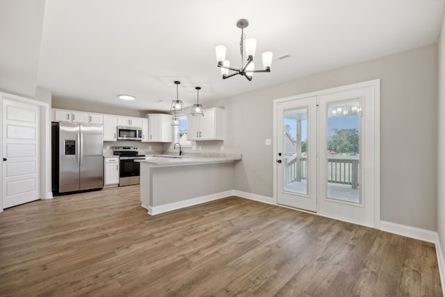 kitchen featuring kitchen peninsula, stainless steel appliances, a chandelier, white cabinetry, and hanging light fixtures