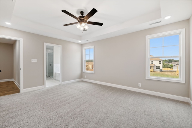 unfurnished bedroom featuring ensuite bathroom, ceiling fan, a raised ceiling, and light colored carpet