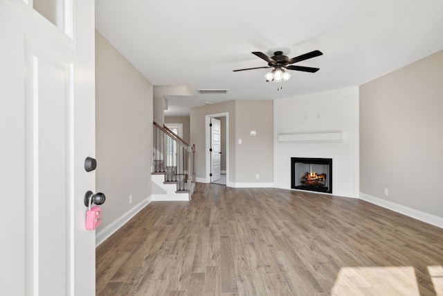 unfurnished living room featuring light wood-type flooring, a large fireplace, and ceiling fan