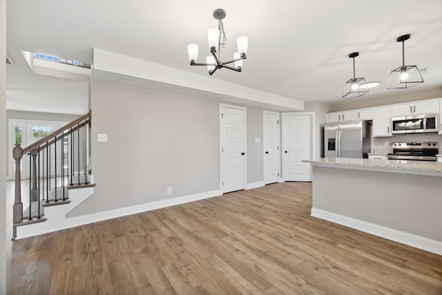 kitchen featuring light stone counters, stainless steel appliances, pendant lighting, white cabinets, and a chandelier