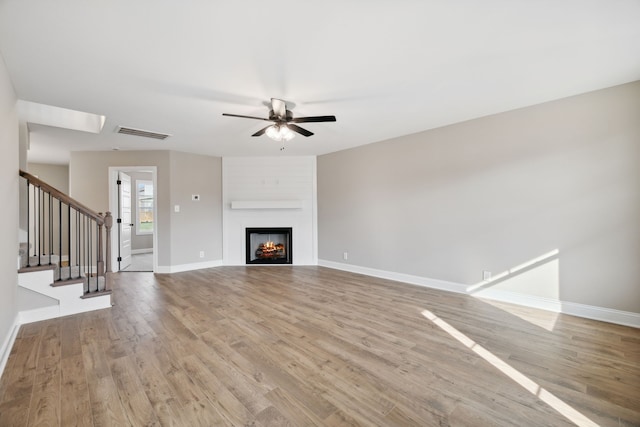 unfurnished living room with ceiling fan, a fireplace, and light hardwood / wood-style flooring