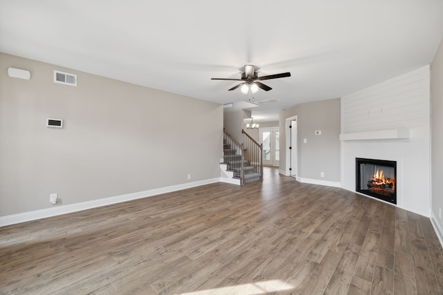 unfurnished living room with ceiling fan with notable chandelier, hardwood / wood-style floors, and a large fireplace