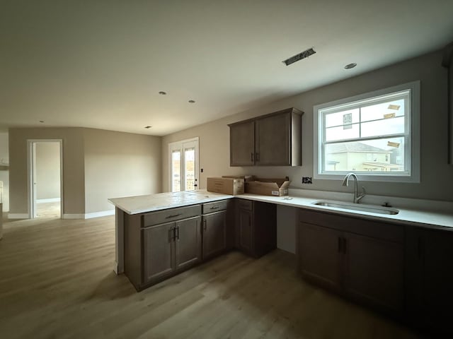 kitchen featuring kitchen peninsula, dark brown cabinets, light hardwood / wood-style floors, and sink