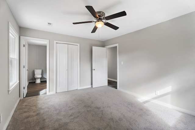 unfurnished bedroom featuring a closet, ceiling fan, connected bathroom, and dark carpet