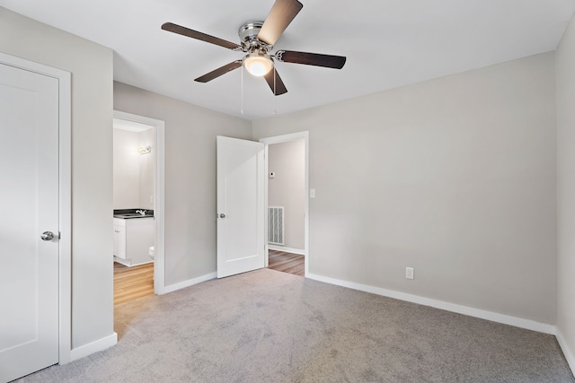 unfurnished bedroom with ceiling fan, ensuite bathroom, and light colored carpet