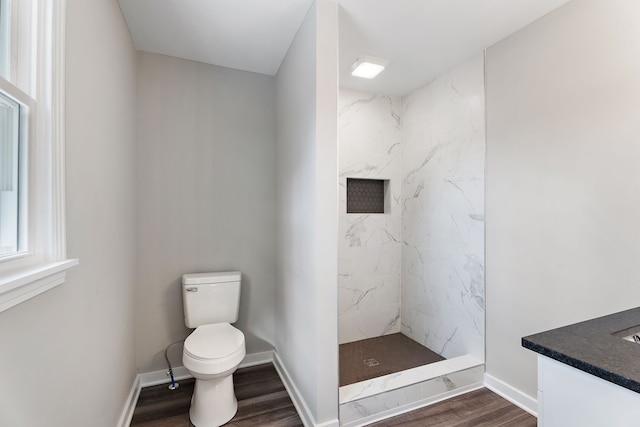 bathroom featuring a tile shower, toilet, wood-type flooring, and vanity