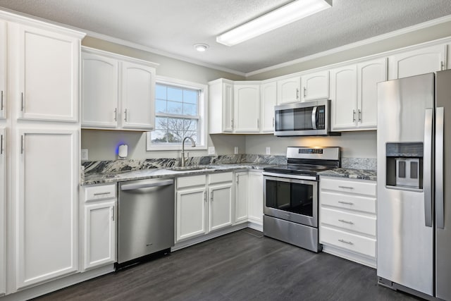 kitchen with appliances with stainless steel finishes, white cabinetry, dark stone counters, and sink