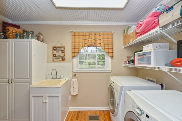 clothes washing area with sink, a skylight, light wood-type flooring, washer and clothes dryer, and cabinets