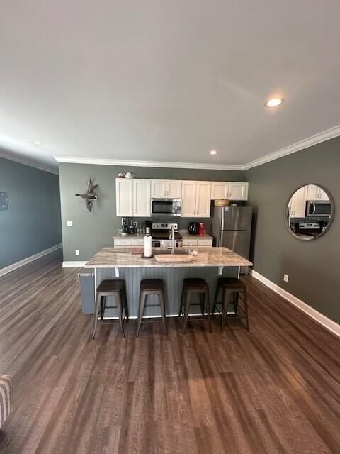 kitchen with appliances with stainless steel finishes, white cabinetry, dark hardwood / wood-style floors, and a kitchen breakfast bar