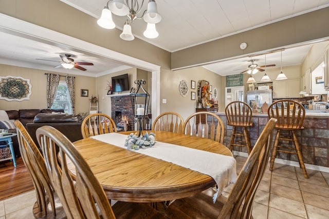 tiled dining space with crown molding, a fireplace, and ceiling fan with notable chandelier