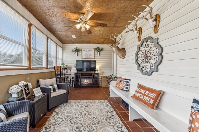 tiled living room featuring wooden walls, a fireplace, and ceiling fan