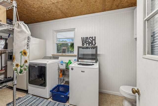 laundry area featuring wood walls, washer and dryer, and light tile patterned floors