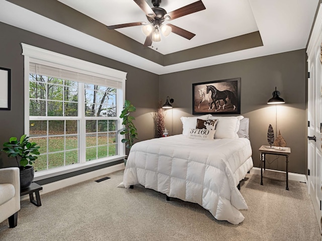 carpeted bedroom with a raised ceiling and ceiling fan