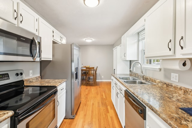 kitchen with appliances with stainless steel finishes, sink, white cabinetry, dark stone countertops, and light hardwood / wood-style flooring