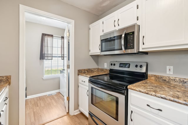 kitchen with white cabinetry, stainless steel appliances, light hardwood / wood-style floors, and dark stone countertops