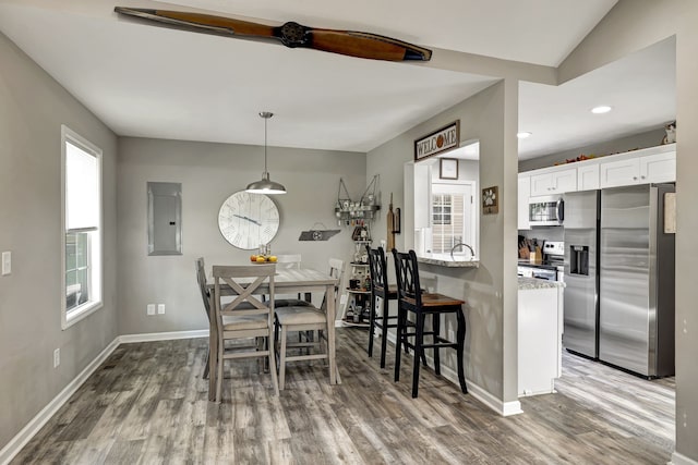 dining area featuring hardwood / wood-style floors, vaulted ceiling, electric panel, and a healthy amount of sunlight