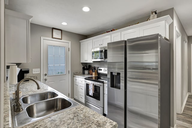 kitchen with stainless steel appliances, hardwood / wood-style floors, sink, white cabinetry, and light stone counters