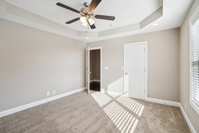 unfurnished bedroom with light carpet, ceiling fan, and a tray ceiling