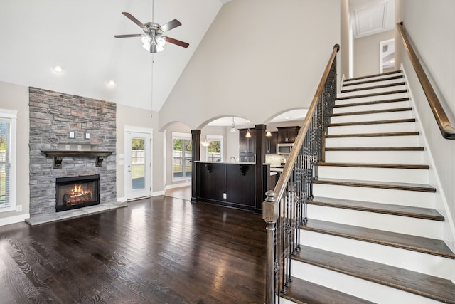 unfurnished living room featuring ceiling fan, dark hardwood / wood-style floors, high vaulted ceiling, a fireplace, and decorative columns