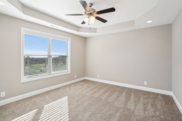 carpeted empty room featuring ceiling fan and a raised ceiling