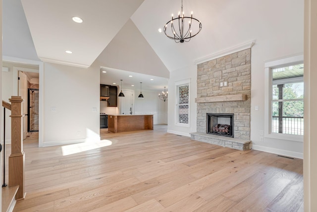 unfurnished living room featuring an inviting chandelier, a stone fireplace, high vaulted ceiling, and light wood-type flooring