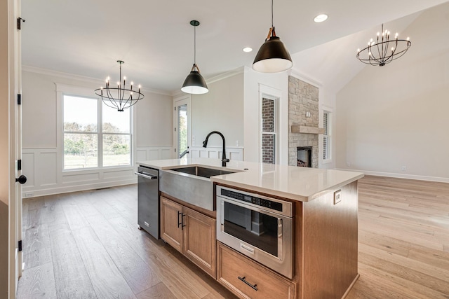 kitchen with a sink, stainless steel dishwasher, light wood-style flooring, and a notable chandelier