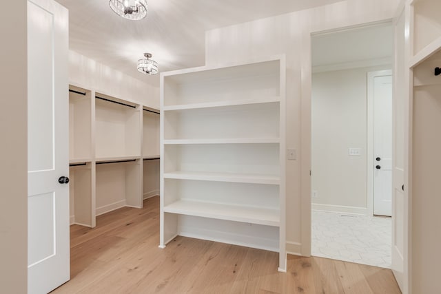 walk in closet with light hardwood / wood-style floors and a chandelier