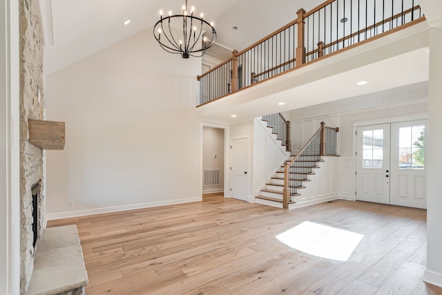 unfurnished living room featuring high vaulted ceiling, light wood-type flooring, french doors, a stone fireplace, and a notable chandelier