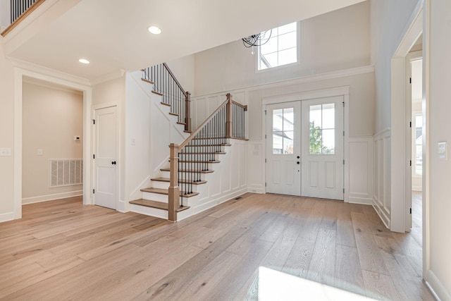 foyer entrance featuring visible vents, a decorative wall, stairway, light wood-style flooring, and a notable chandelier