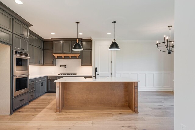 kitchen with a sink, light wood-style floors, light countertops, double oven, and an island with sink