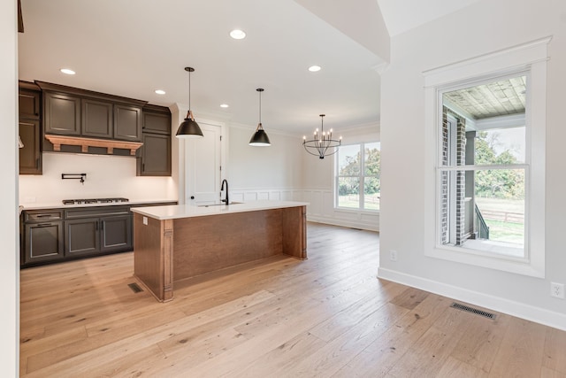 kitchen featuring dark brown cabinetry, decorative light fixtures, a notable chandelier, light hardwood / wood-style flooring, and a kitchen island with sink