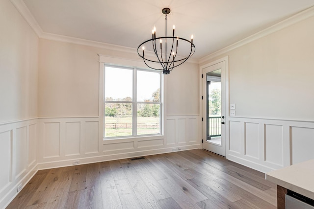 unfurnished dining area with an inviting chandelier, crown molding, wood finished floors, and a healthy amount of sunlight