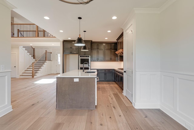kitchen with crown molding, a decorative wall, a center island with sink, light wood-type flooring, and light countertops