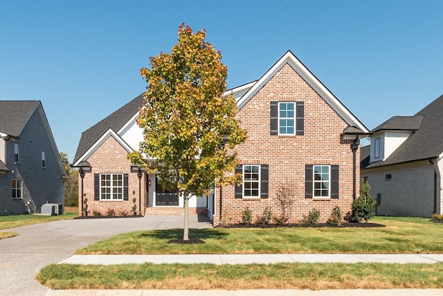view of front of home with concrete driveway, brick siding, cooling unit, and a front lawn