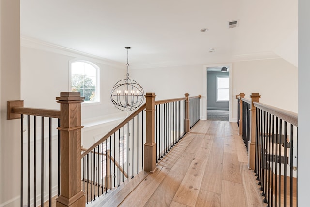 hall with a notable chandelier, ornamental molding, plenty of natural light, and light wood-type flooring