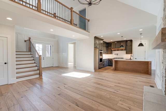 unfurnished living room featuring light wood-type flooring, a sink, a high ceiling, a decorative wall, and stairs