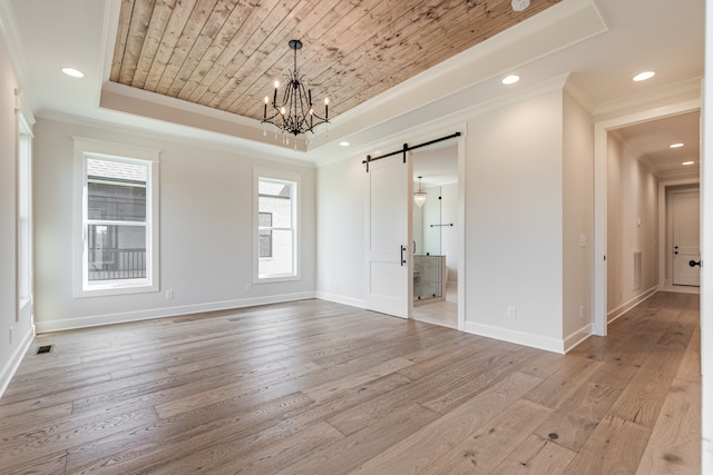 unfurnished room with a wealth of natural light, a barn door, a tray ceiling, and light hardwood / wood-style floors