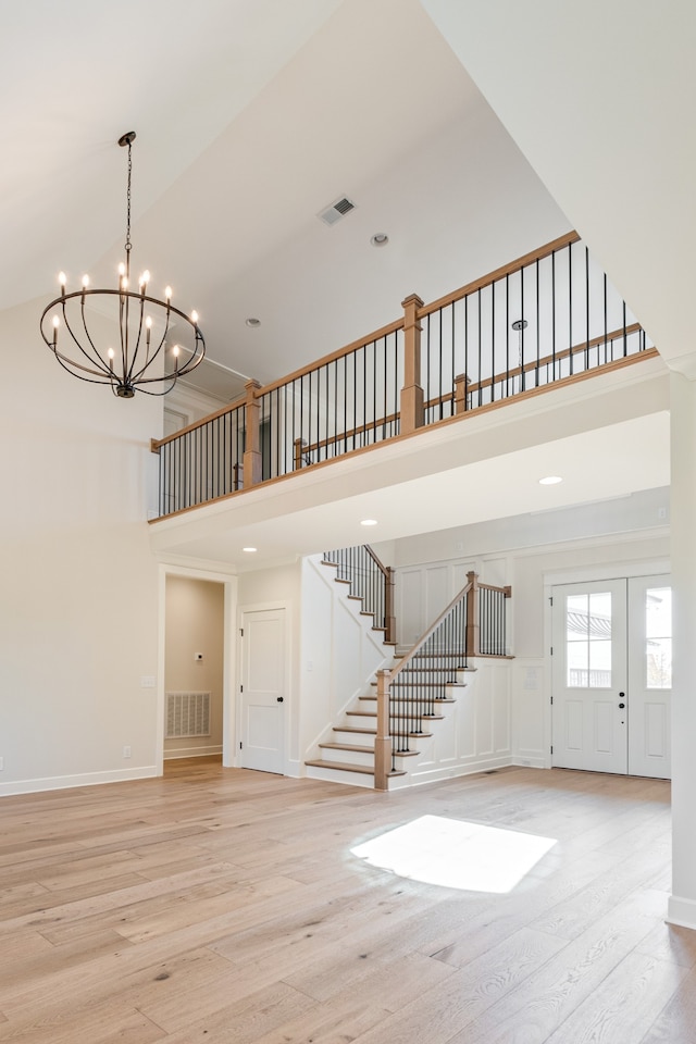 unfurnished living room featuring a chandelier, light hardwood / wood-style flooring, and a towering ceiling