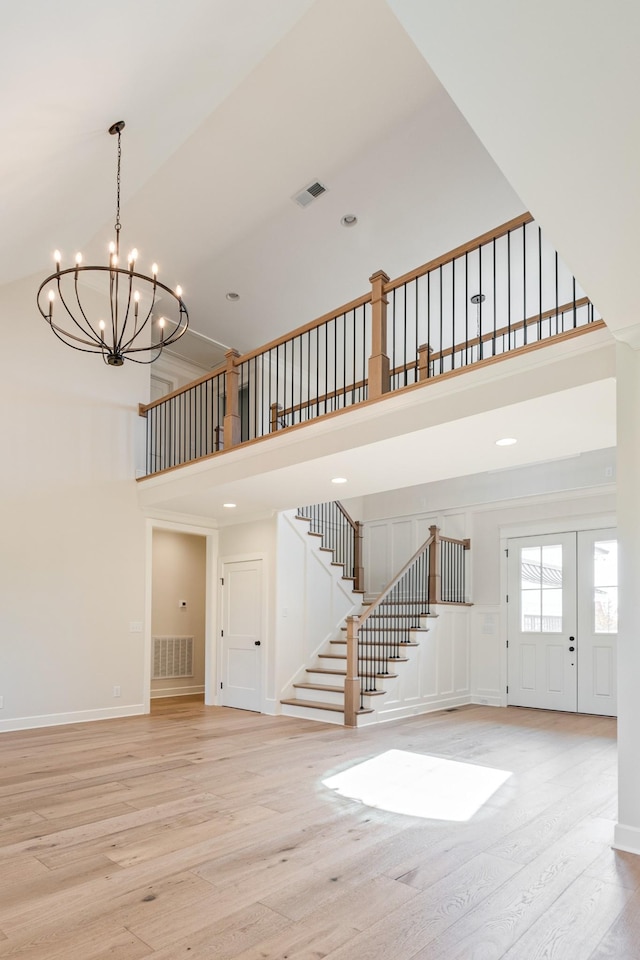 unfurnished living room with visible vents, light wood finished floors, a notable chandelier, a high ceiling, and stairs