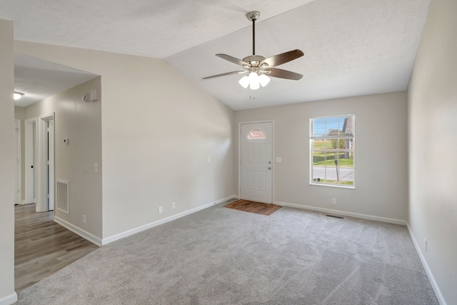 spare room featuring a textured ceiling, ceiling fan, light wood-type flooring, and vaulted ceiling